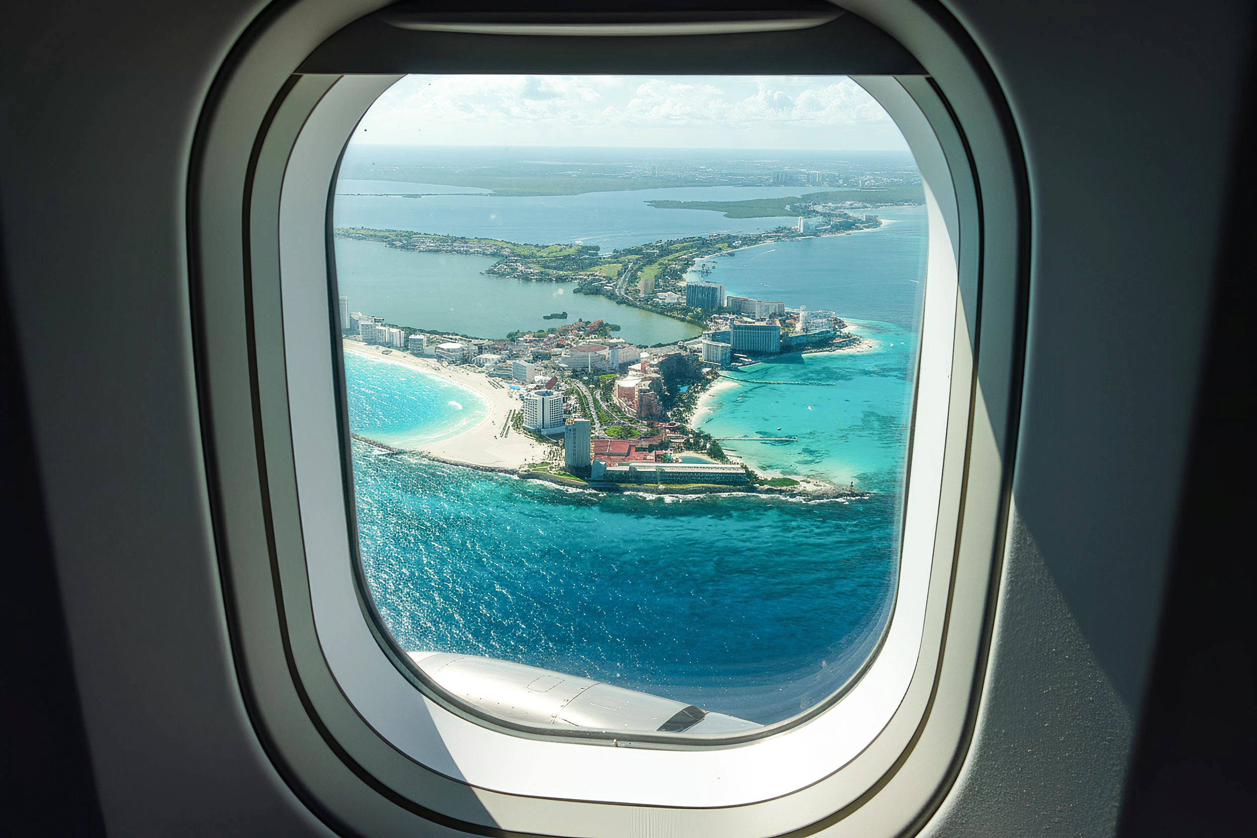 Aerial view of Cancún’s hotel zone and turquoise coastline seen through an airplane window.