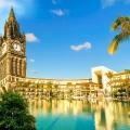 A scenic view of a hotel resort with a clock tower and palm trees, showing the outdoor pool area.