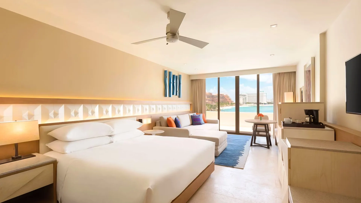 A modern hotel room at Hyatt Ziva Cancun with a king bed, a sofa bed, a flat-screen TV, and a large glass door opening to an ocean-view balcony.