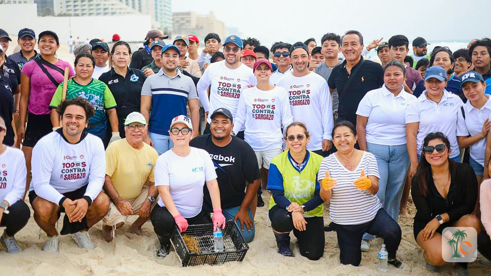 A large group of diverse volunteers and local officials posing together during a sargassum beach cleanup initiative in Cancun.
