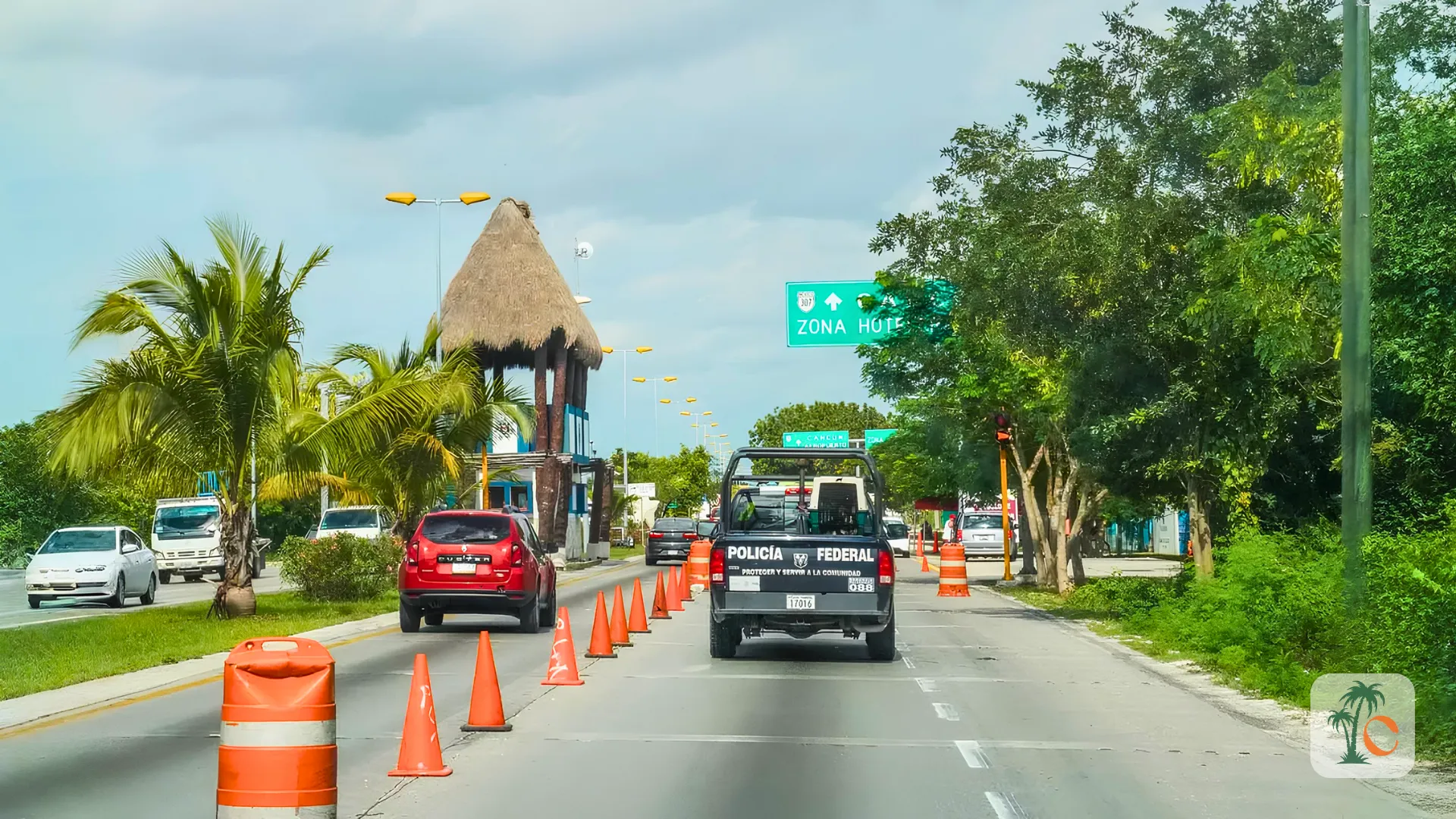 A federal police vehicle driving down a road in Cancun, passing traffic cones and a sign for the Hotel Zone, with lush greenery on either side.
