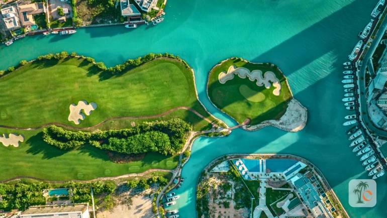 Aerial view of a golf course with a winding waterway, luxury yachts docked along the marina, and modern residential buildings surrounding the area in Cancun, reflecting the city's strategic urban development.